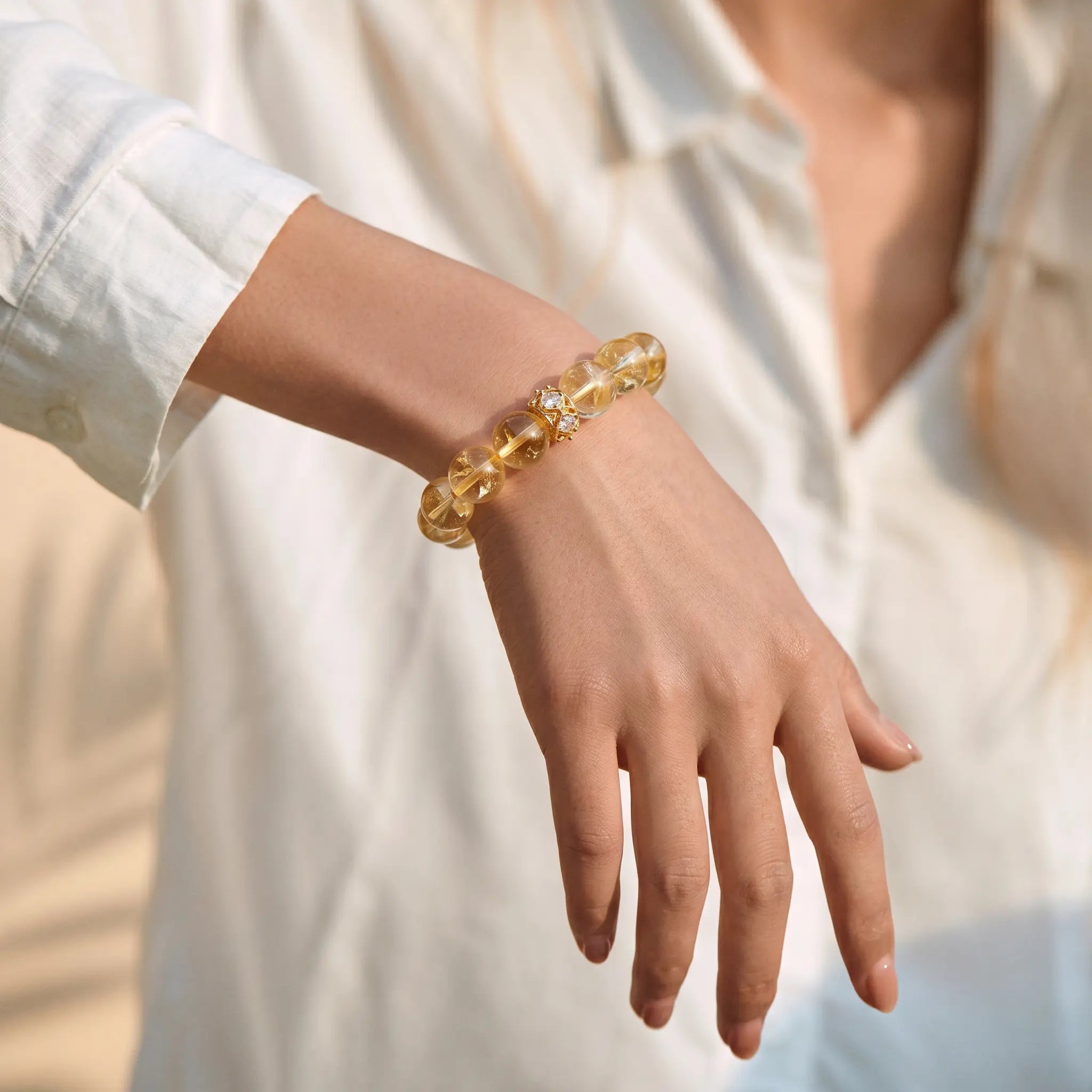 Close-up shot of a female right hand raised naturally downward displaying a glowing yellow citrine bracelet.