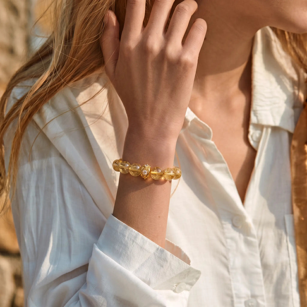 Cropped upper body shot to the earlobe showing a woman right forearm with a hand touching the earlobe to display a crystal bracelet.