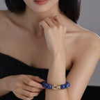 Front close-up view from collarbone to chest showing a woman right wrist wearing the Tranquil Lapis Bracelet with left fingers gently touching the centerpiece.