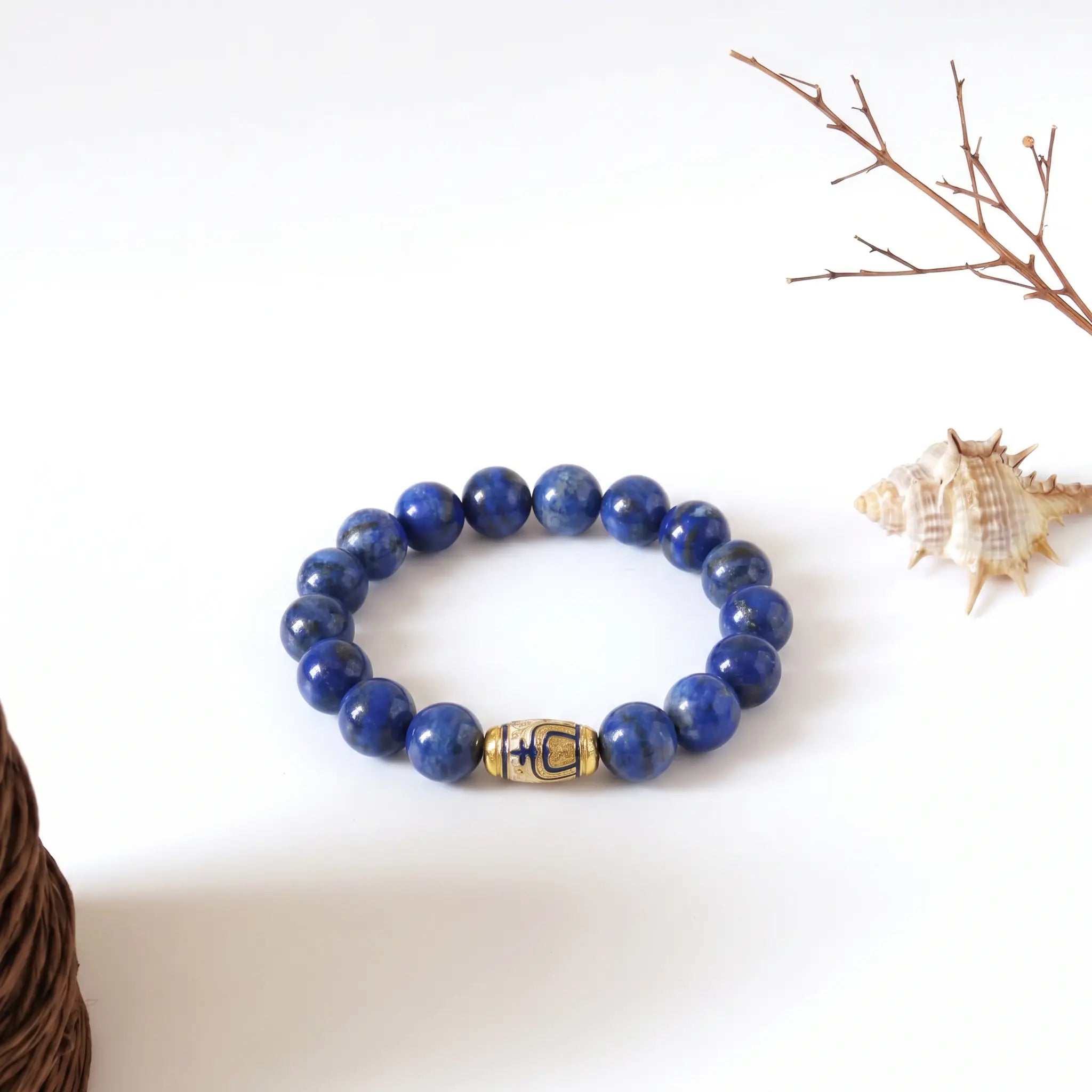 Tranquil Lapis Bracelet displayed flat on a clean white surface with a rustic conch shell and dry branch decoration.