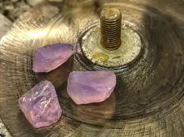 Beveling and shaping raw gemstone pieces on a grinding wheel during the handmade jewelry process.