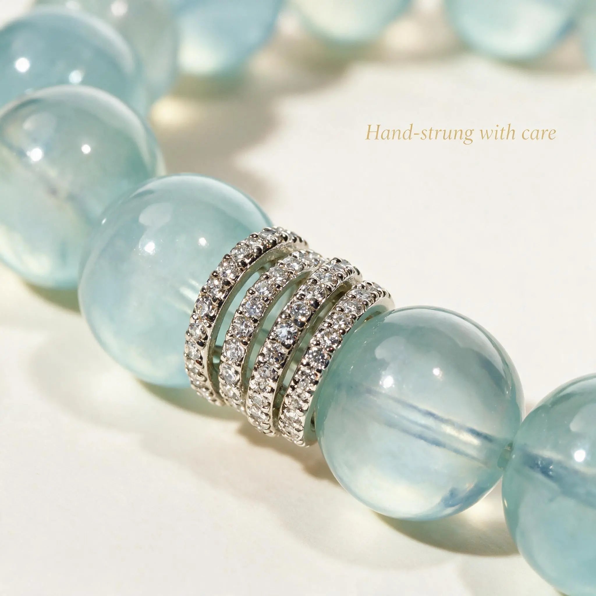 Front view portrait up to collarbone of a lady raising her left forearm to display an aquamarine bracelet touched by her right hand.